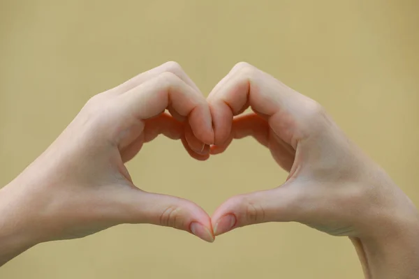 Woman making heart with hands on beige background, closeup