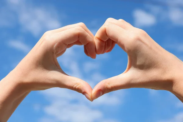 Woman making heart with hands against blue sky, closeup