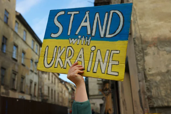 stock image Young woman holding poster in colors of national flag and words Stand with Ukraine outdoors, closeup