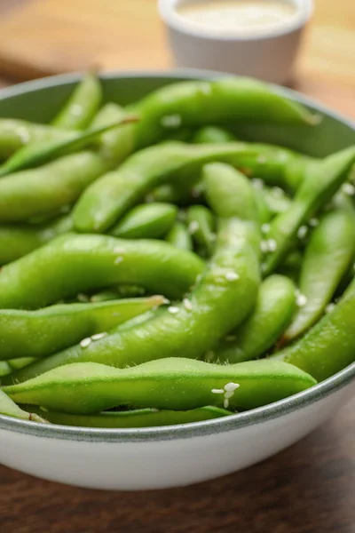 Bowl with green edamame beans in pods on wooden table, closeup