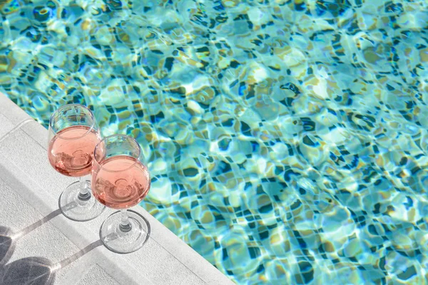 stock image Glasses of tasty rose wine on swimming pool edge, space for text