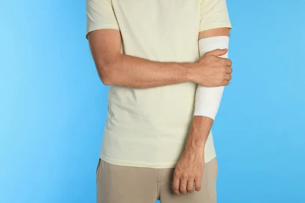 Man with arm wrapped in medical bandage on light blue background, closeup