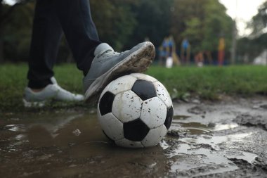 Açık hava birikintisinde kirli futbol topu olan adam, yakın plan.