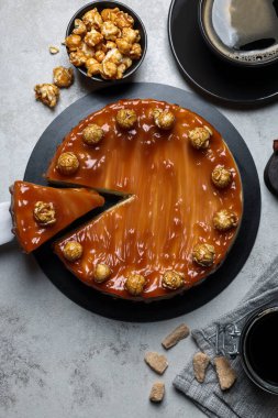 Sliced delicious caramel cheesecake with popcorn served on light grey table, flat lay
