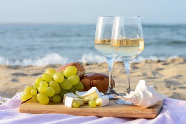 Beyaz şaraplı bardaklar ve kumlu deniz kıyısında piknik için atıştırmalıklar.