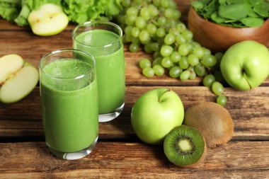 Bardakta yeşil smoothie ve ahşap masada taze malzemeler.