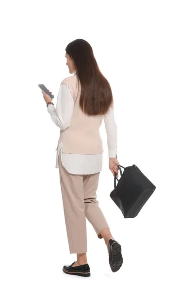 スタイリッシュな革のバッグと白い背景を歩くスマートフォンを持つ若い女性 — ストック写真
