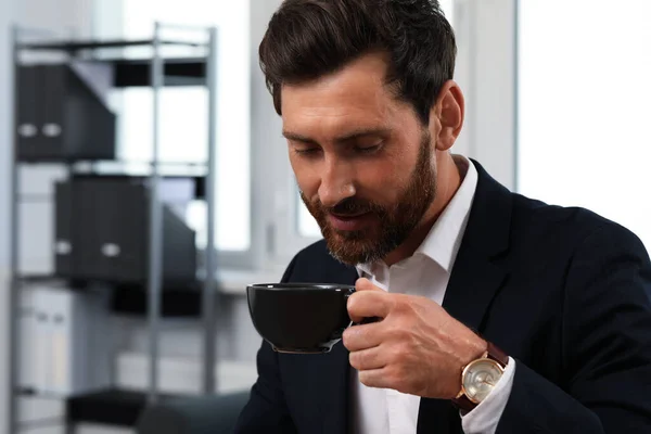 Handsome bearded man drinking cup of coffee indoors