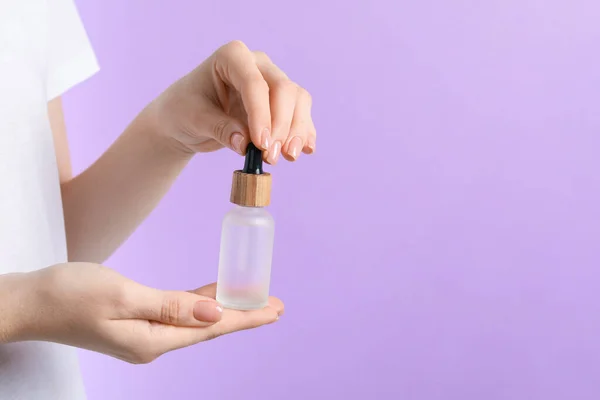 Woman holding bottle with serum against lilac background, closeup. Space for text