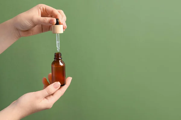 stock image Woman dripping serum from pipette into bottle against olive background, closeup. Space for text