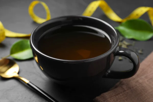Cup of herbal diet tea on black table, closeup. Weight loss concept