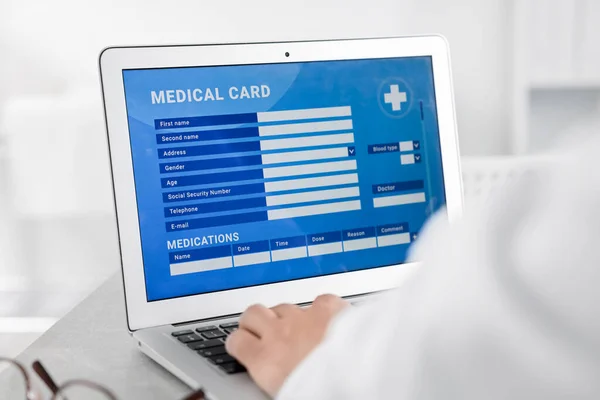 病院のテーブルで患者の医療カードを記入するためにラップトップを使用して医師 クローズアップ — ストック写真