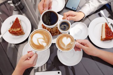 Açık kafedeki ahşap masada kahve içen arkadaşlar.