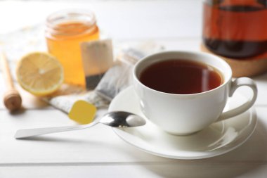 Çay poşetleri, şeker ve limon beyaz ahşap masada sıcak içecek bardağının yanında.