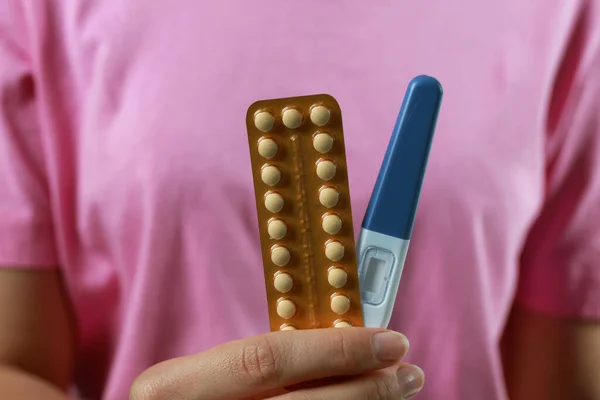 Woman holding birth control pills pregnancy test, closeup