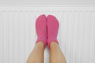 Beyaz duvarın yanındaki ısıtma kaloriferinde bacakları ısıtan kadın, yakın plan.