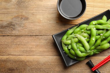 Ahşap masada soya sosuyla servis edilen kabuklu yeşil edamame fasulyeleri. Metin için boşluk