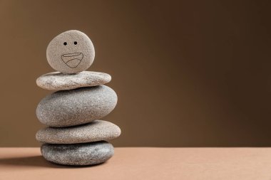 Masada çizilmiş gülen yüzlü taş yığını koyu bej arka planda, yazı için yer var. Zen kavramı