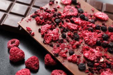 Farklı çikolatalar, dondurulmuş meyveler siyah tabakta, yakın plan.