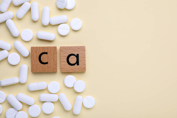 Wooden cubes with symbol Ca (Calcium) and pills on beige background, top view. Space for text