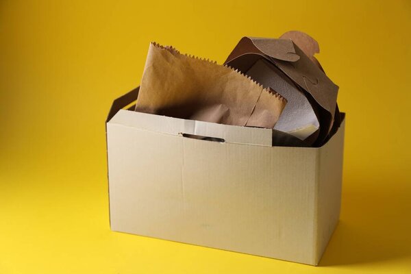 Box with waste paper on yellow background