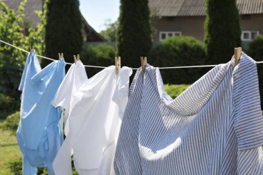 Clean clothes hanging on washing line in garden, closeup. Drying laundry