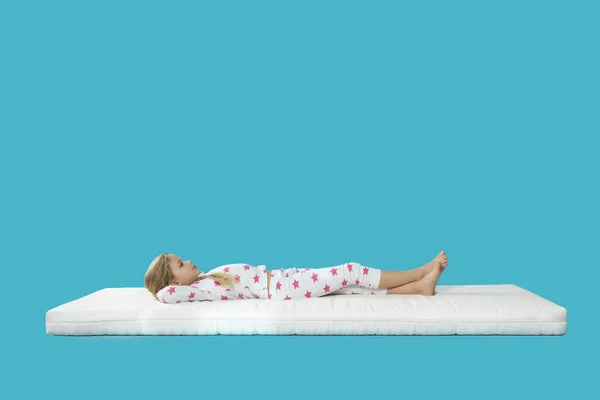 Açık Mavi Arka Planda Rahat Bir Yatakta Uzanan Küçük Kız — Stok fotoğraf