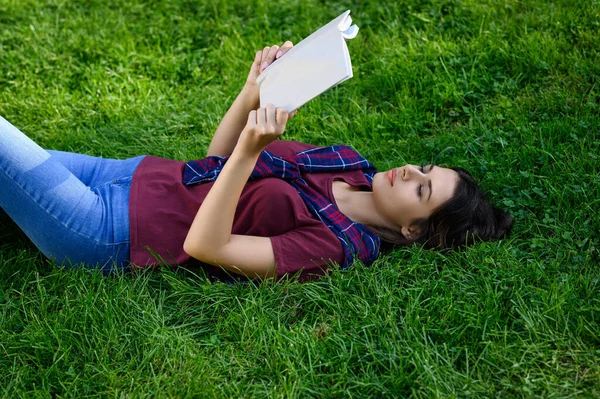 年轻女子躺在草地上看书 — 图库照片