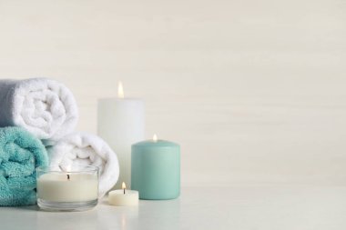 Beyaz masa üzerinde yanan mumlar ve rulo havlular olan güzel bir spa kompozisyonu. Metin için boşluk