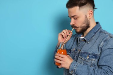 Yakışıklı genç adam açık mavi arka planda cam şişeden meyve suyu içiyor. Metin için boşluk