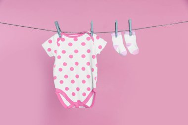 Bebek tulumu ve çorapları pembe arka planda çamaşır ipinde kuruyor.