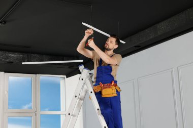 Üniformalı elektrikçi tavan lambası yerleştiriyor.