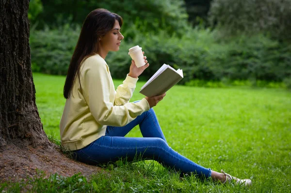 Ung Kvinna Med Kopp Kaffe Läsa Bok Nära Träd Parken — Stockfoto