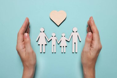 Açık mavi arka planda aile ve kalp figürlerini koruyan bir kadın. Sigorta konsepti