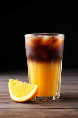 Tasty refreshing drink with coffee and orange juice on wooden table against dark background clipart