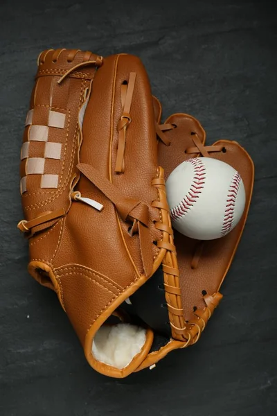 Catcher\'s mitt and baseball ball on black slate background, top view. Sports game