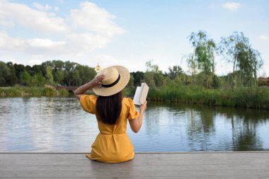 Göl kenarındaki iskelede kitap okuyan kadın.