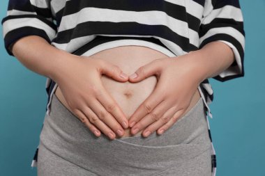 Pregnant woman on light blue background, closeup