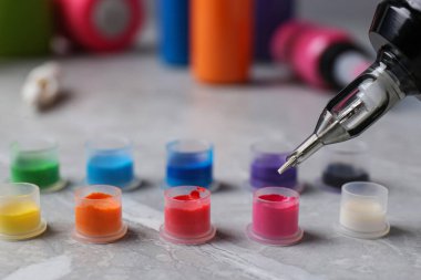 Dövme makinesinin iğnesini açık gri masadaki mürekkebe batırıyorum. Yakın plan.