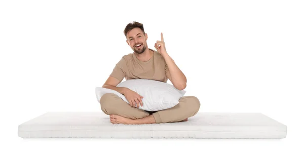 stock image Man with pillow sitting on soft mattress and pointing upwards against white background