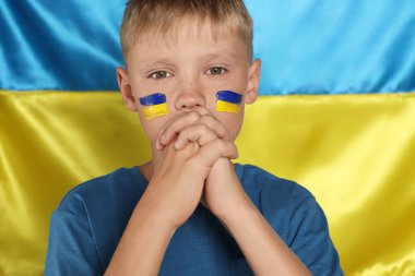 Ukrayna bayrağının yanında elleri bağlı dua eden küçük bir çocuk. Savaş konsepti yok