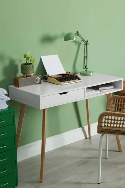 Writer's workplace with typewriter on wooden desk near pale green wall in room