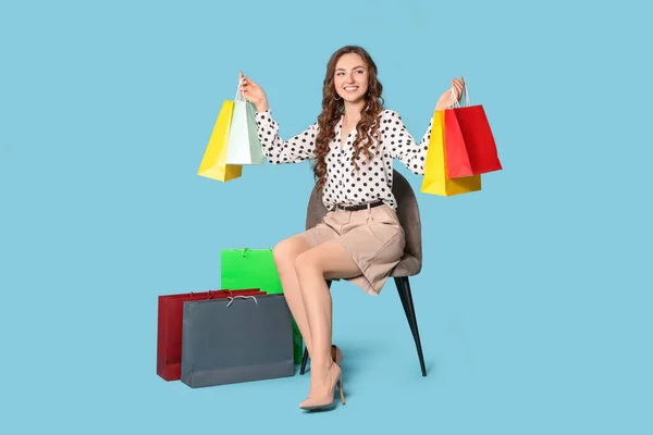 Glückliche Frau Mit Bunten Einkaufstaschen Auf Stuhl Vor Hellblauem Hintergrund — Stockfoto