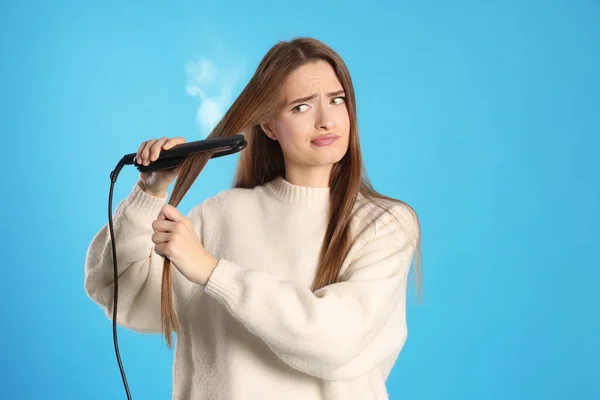 Rozrušená Mladá Žena Zploštělým Železem Světle Modrém Pozadí Poškození Vlasů — Stock fotografie