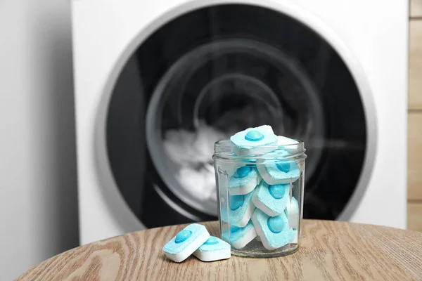 Jar with water softener tablets on wooden table near washing machine