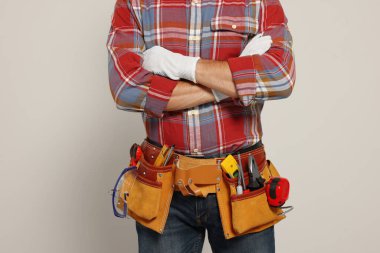 Professional builder with tool belt on light background, closeup