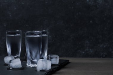 Siyah duvara karşı ahşap masanın üzerinde buz küpleri olan votka kadehleri. Metin için boşluk