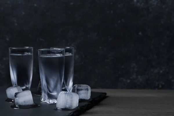 Bicchieri Vodka Con Cubetti Ghiaccio Tavolo Legno Contro Parete Nera — Foto Stock