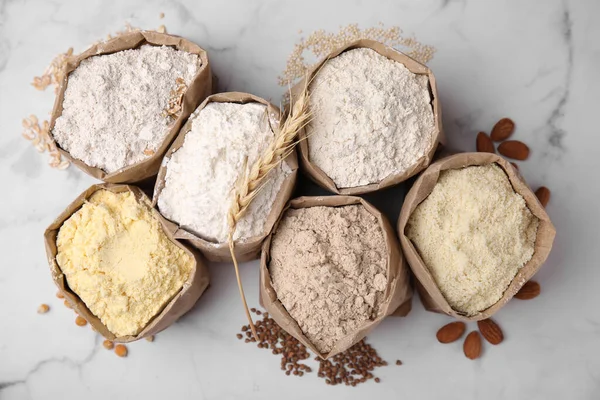 stock image Paper bags with different types of flour and ingredients on white marble table, flat lay