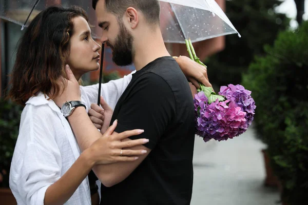 Young couple with umbrella enjoying time together under rain on city street